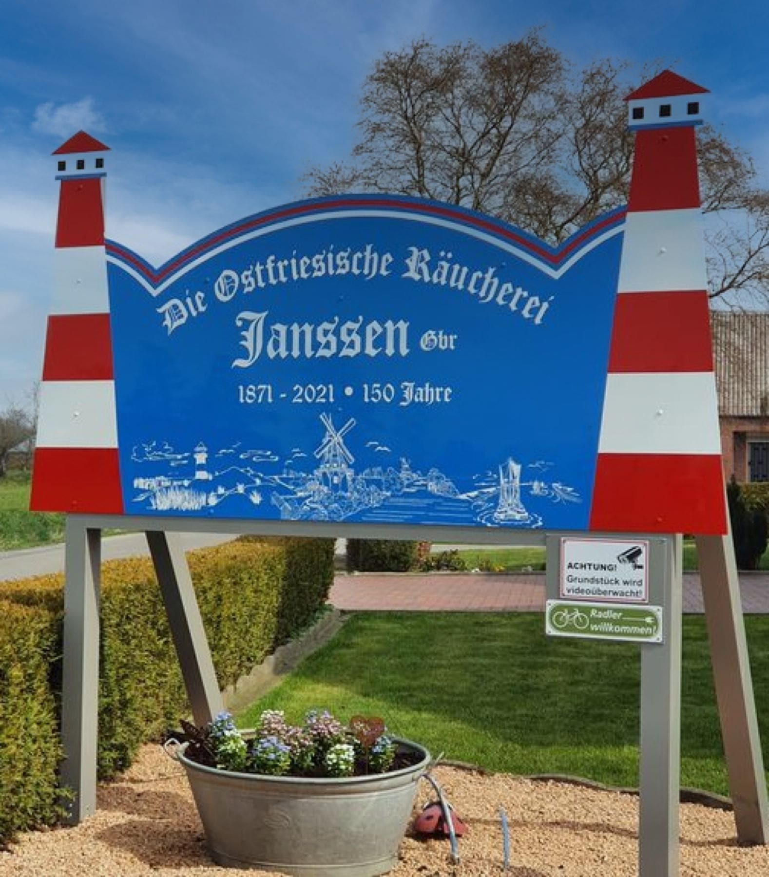 Das blaue Schild an der Einfahrt mit zwei rot-weißen Leuchttürmen.